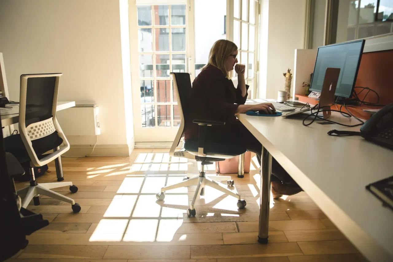 A member of the team at work at a desk in the office, by a sunlit window.
